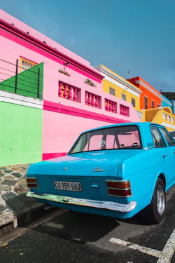 blue sedan parked beside pink and yellow painted building