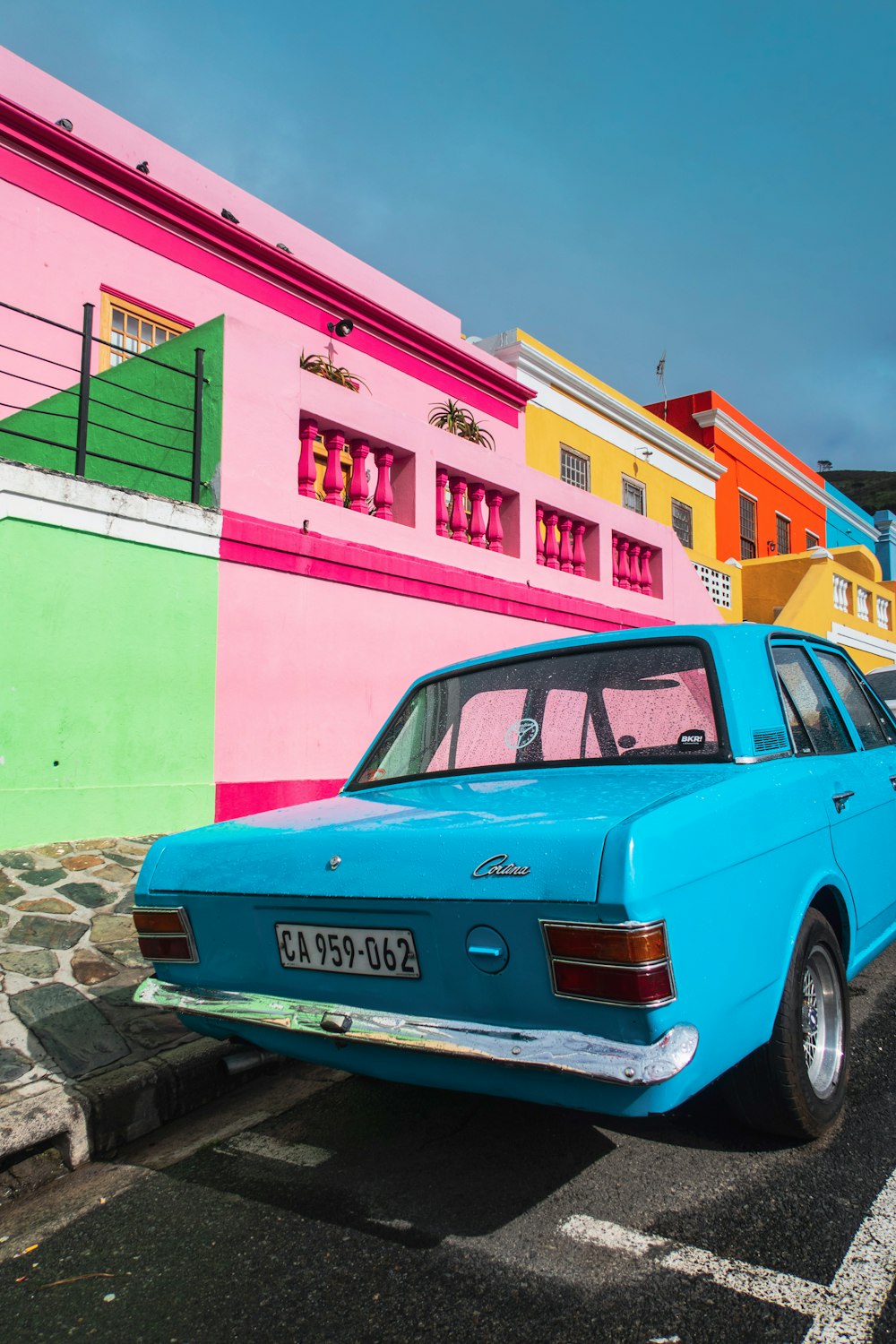 blue sedan parked beside pink and yellow painted building