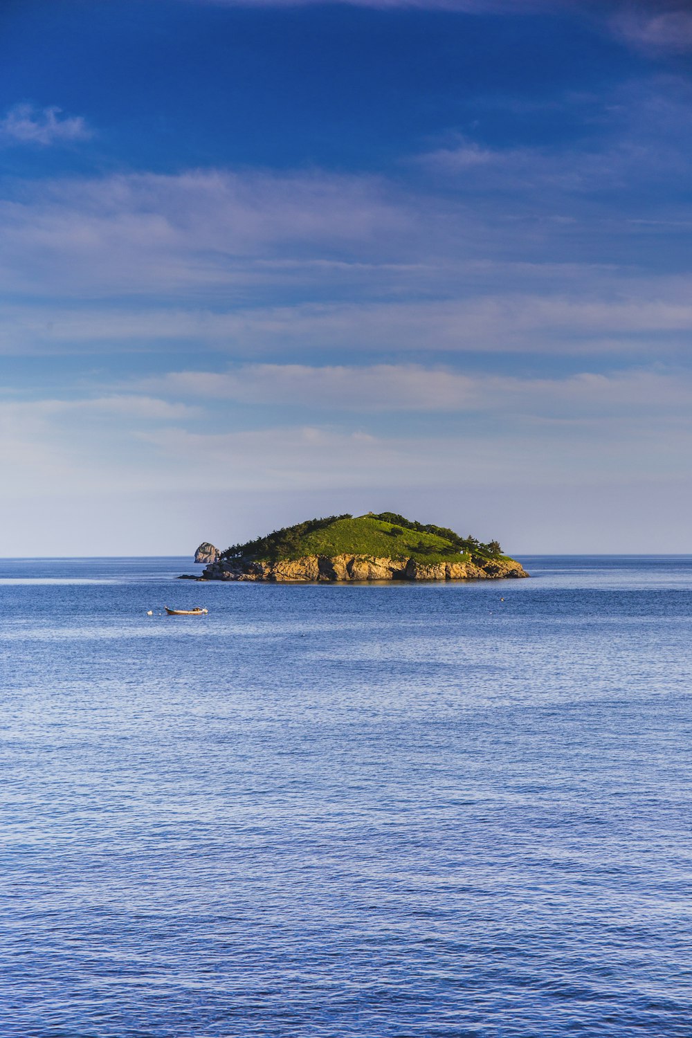 green island on blue sea under white clouds and blue sky during daytime