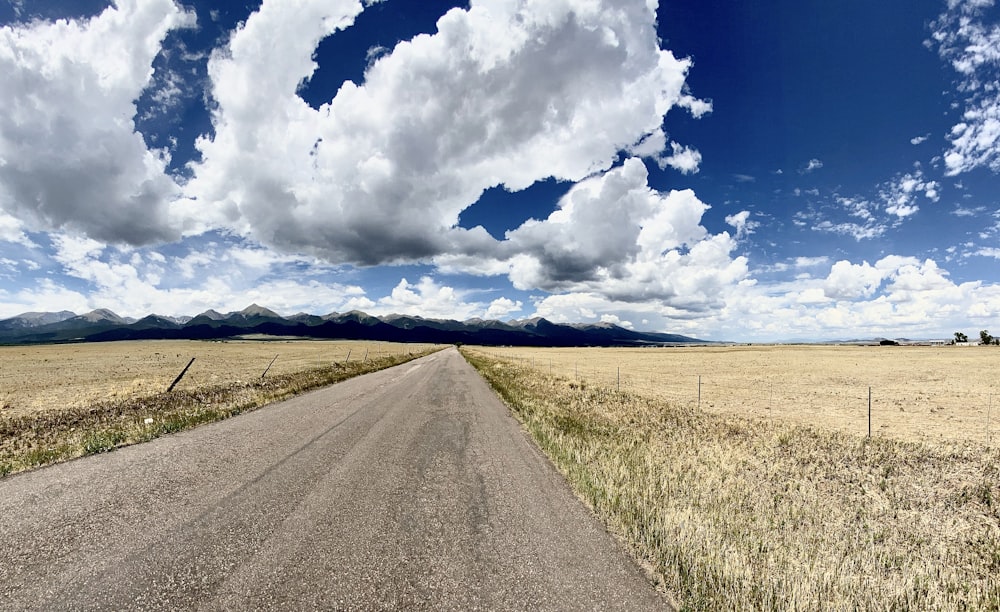 gray asphalt road under blue sky and white clouds during daytime