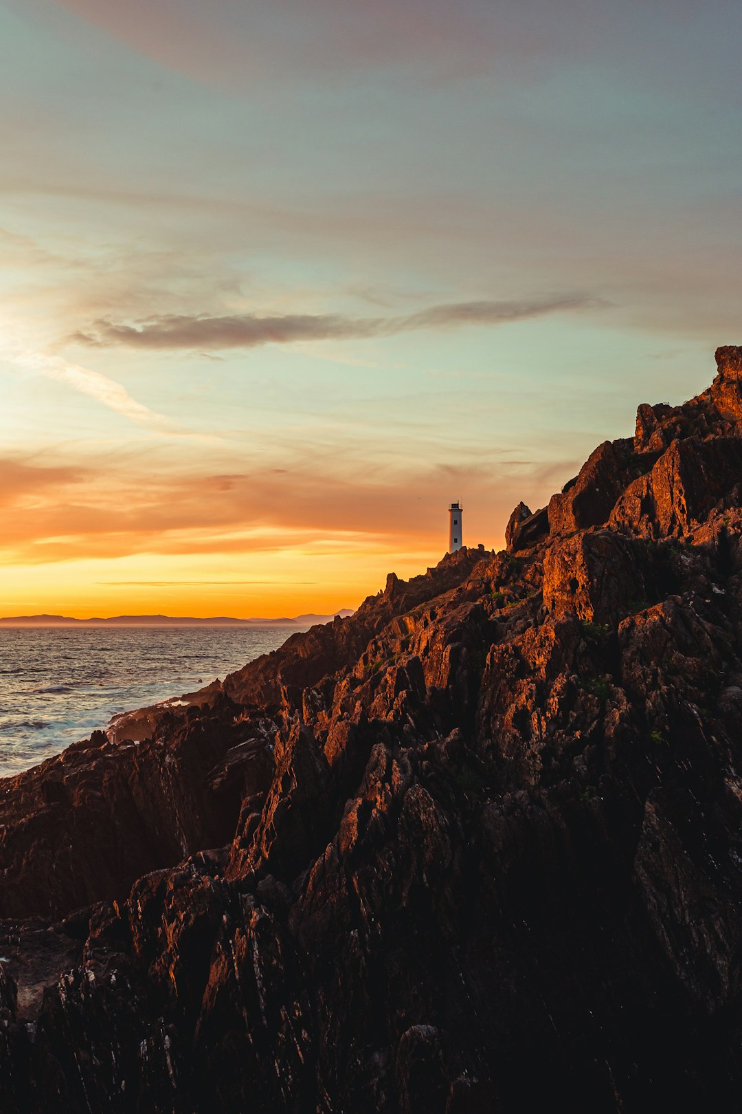 silhouette of lighthouse on cliff by the sea during sunset