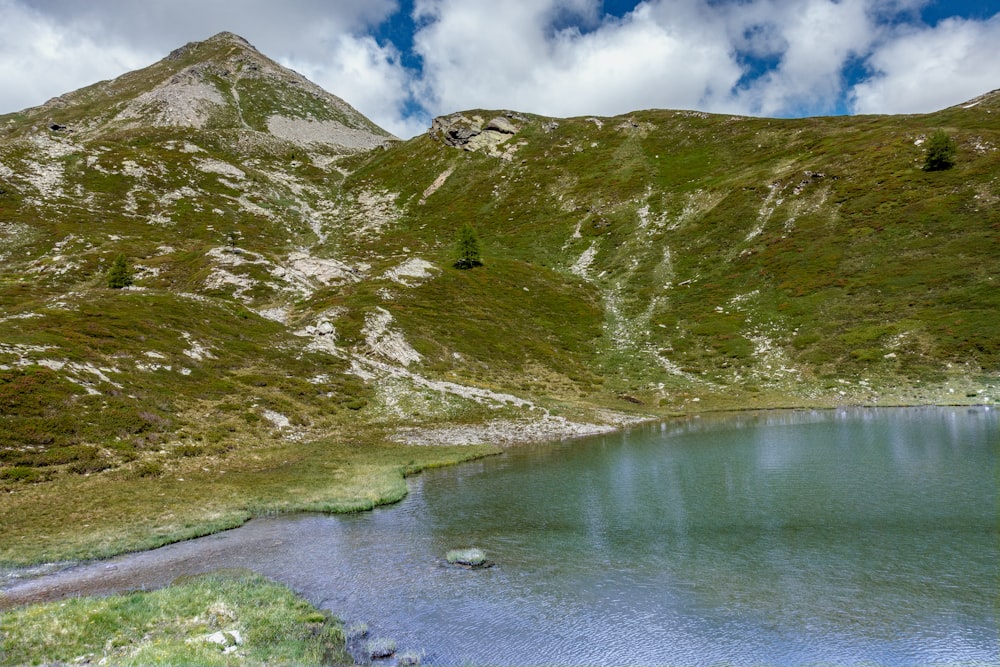 green and gray mountain beside body of water under blue sky during daytime