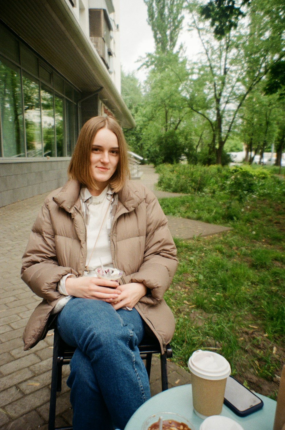 昼間、緑の芝生に座る茶色のコートを着た女性