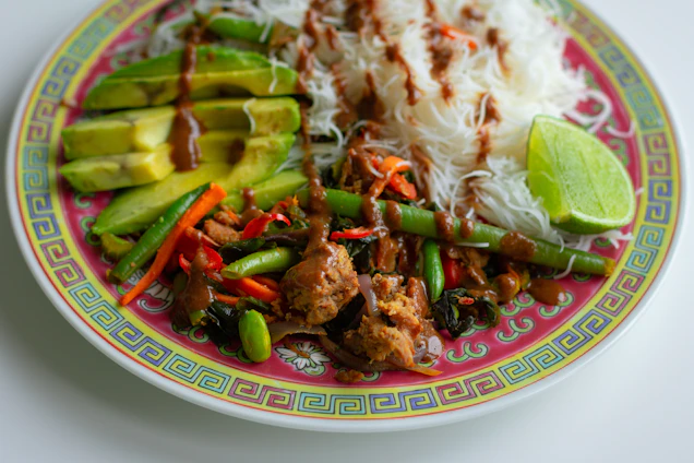 A vibrant plate showcasing a colorful Asian fusion dish with fresh herbs and a drizzle of sauce.