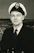 A professional headshot of a confident maritime industry executive in a navy blazer with a subtle ocean background.