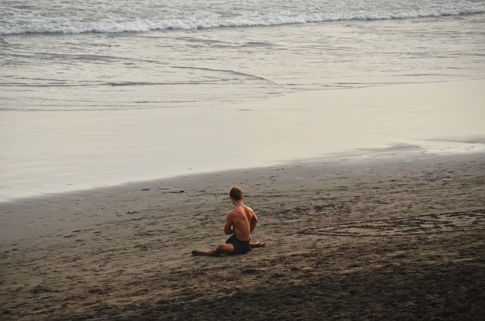 topless boy sitting on beach during daytime