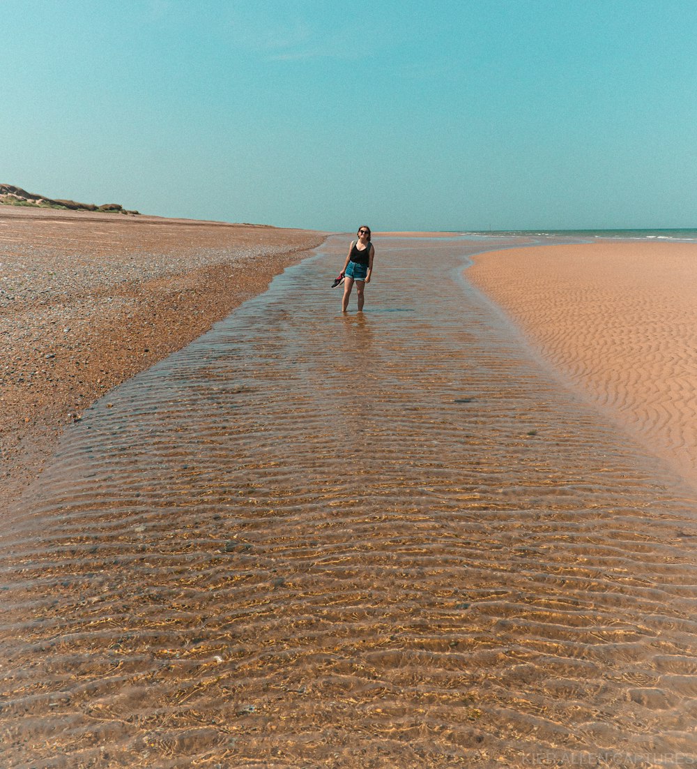 donna in camicia nera che cammina sulla sabbia marrone durante il giorno