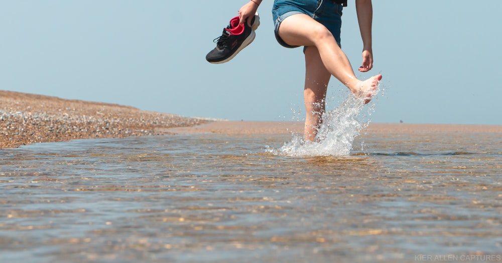 man in black shorts and black and red nike sneakers jumping on water during daytime