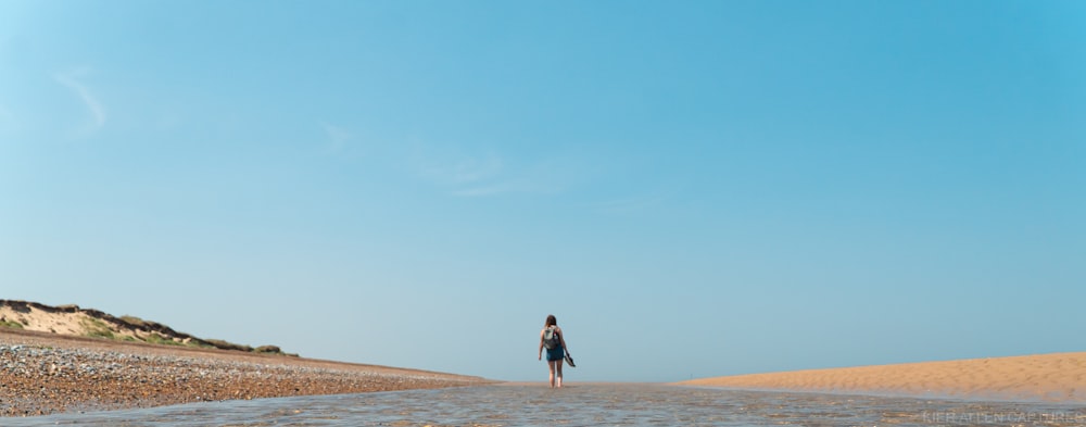 donna in vestito nero che cammina sulla sabbia marrone durante il giorno