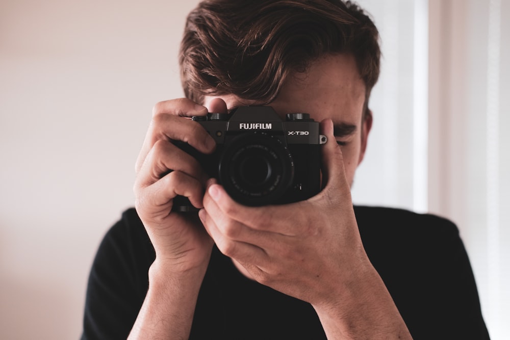 man in black shirt holding black nikon dslr camera