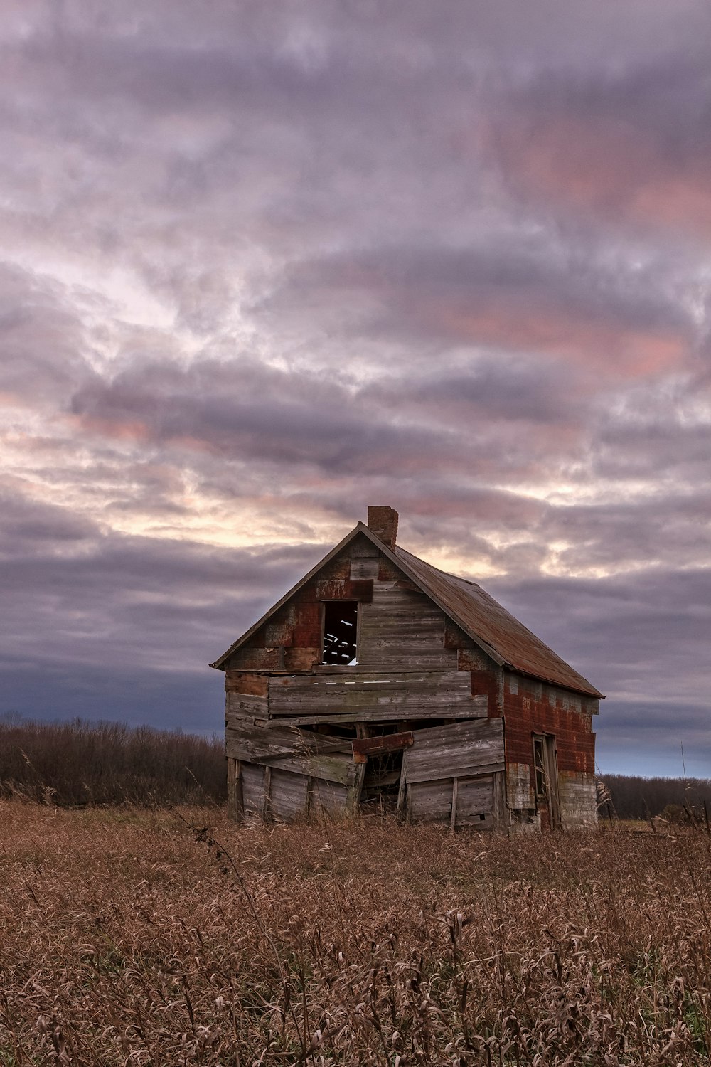 grange en bois brun sur un champ d’herbe brune sous des nuages gris