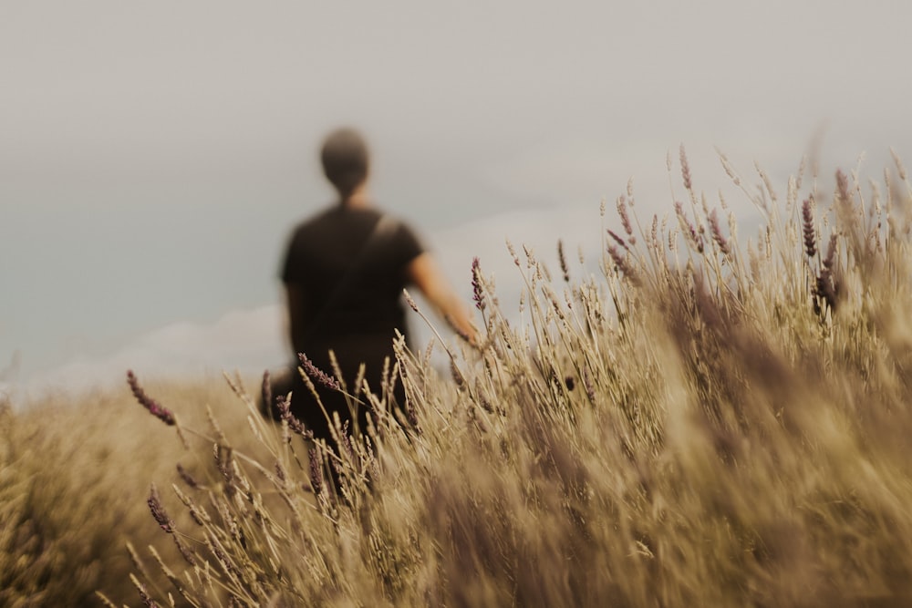 homme en chemise noire debout sur un champ d’herbe brune pendant la journée