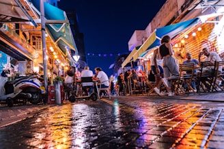 A lively street scene at night with people dancing and chatting outside a cozy urban café
