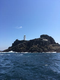 A rocky coastline with crashing waves and a lighthouse standing tall against the horizon.