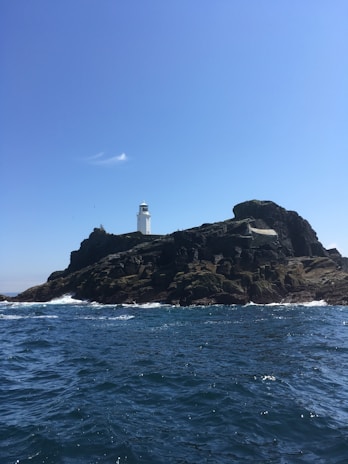 A rocky coastline with crashing waves and a lighthouse standing tall against the horizon.