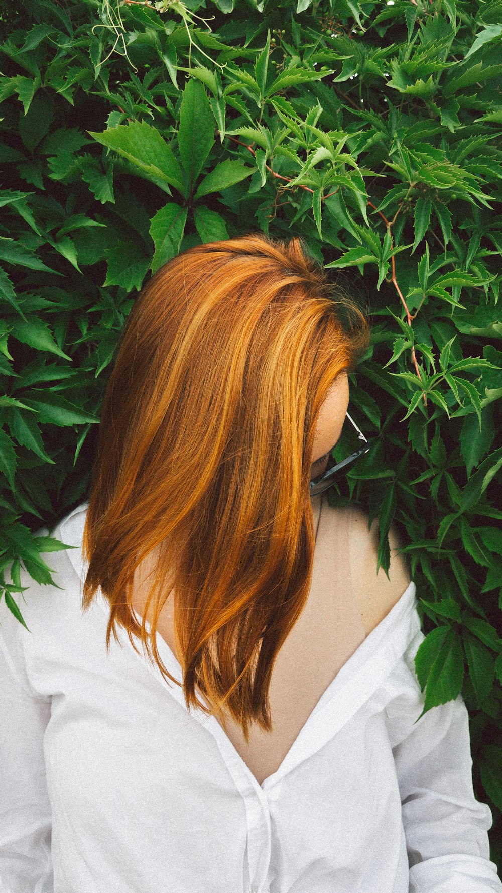 Mujer con camisa blanca de pie cerca de una planta verde