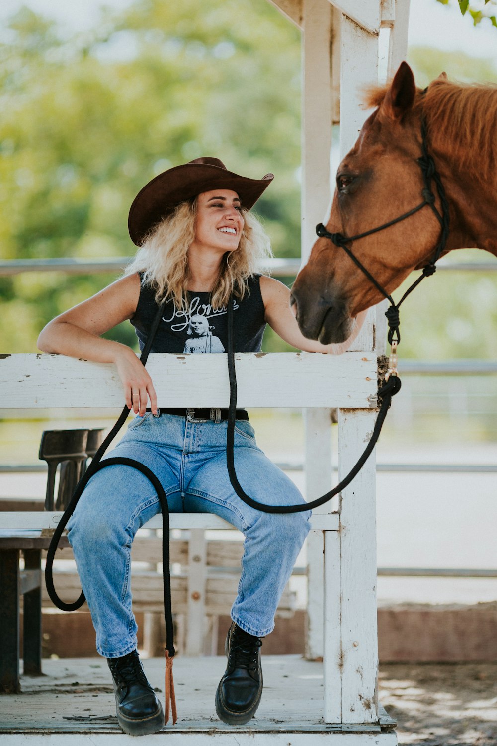 girl in black tank top and blue denim jeans sitting on white wooden fence beside brown