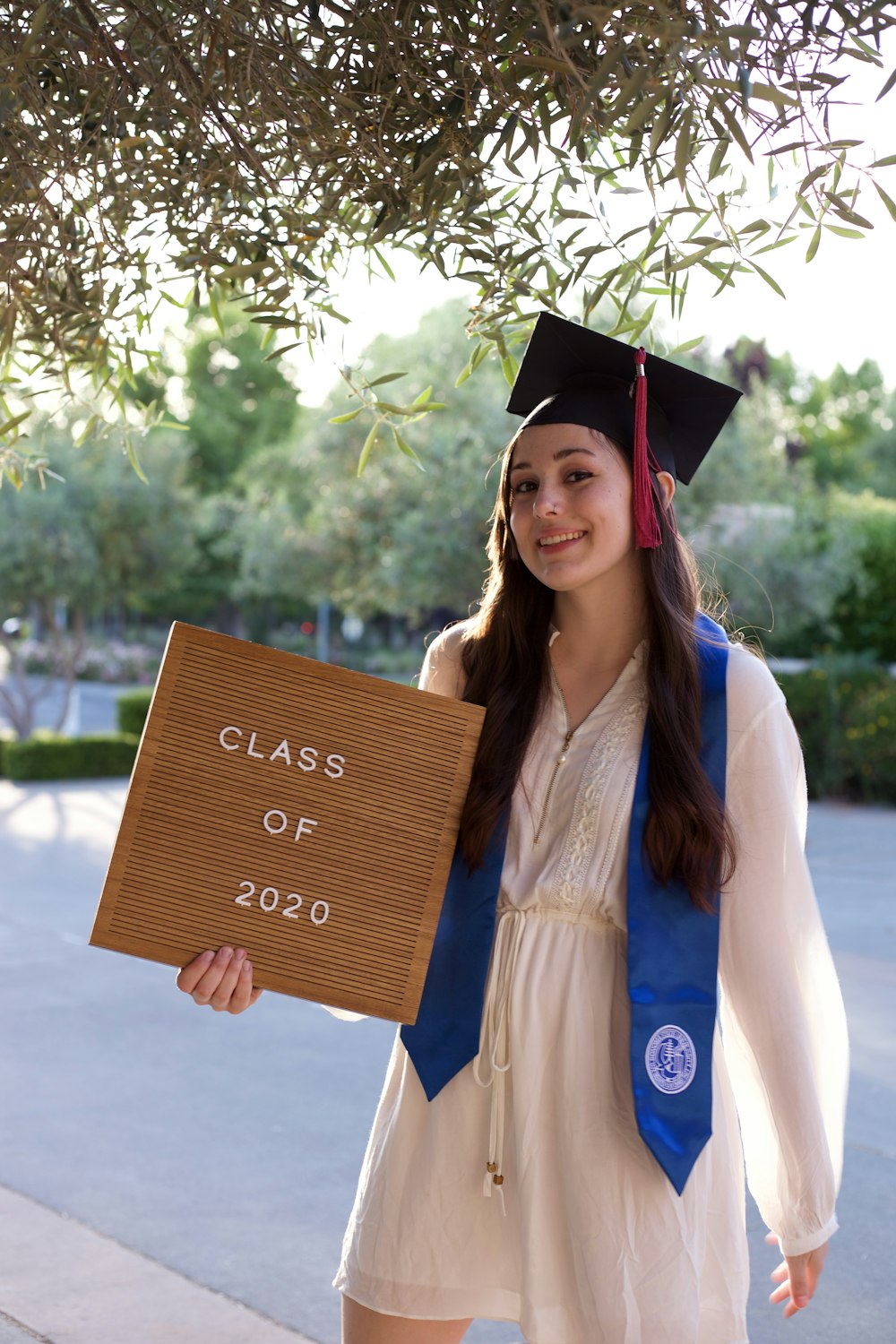 Mujer en toga académica azul sosteniendo tablero de madera marrón