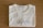 A folded white T-shirt with a stylish logo printed in black on the front. The brand label at the neckline reads 'Vanny Clothing Co.' The shirt lies on a wooden surface, which serves as a simple backdrop.