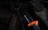 A serrated knife with an orange and black handle lies on a grill grate, alongside a used barbecue grill brush with bristles. The scene is dark, with a focus on the textures of the metal and bristles, creating a rustic and rugged feel.