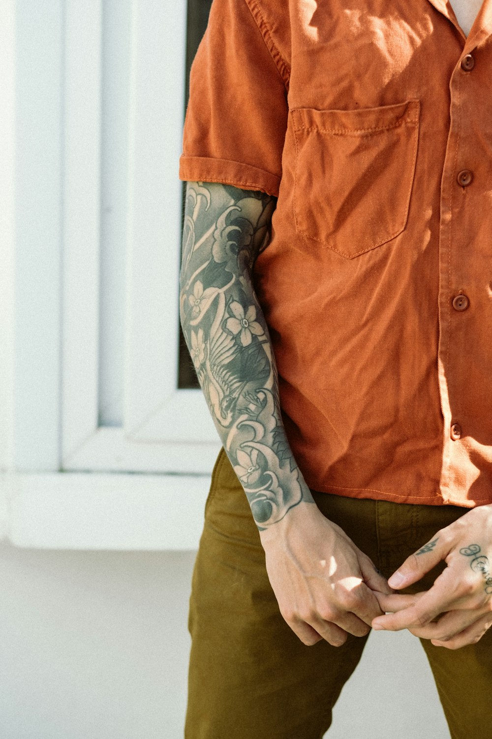 Mann in orangefarbenem Button-Up-Shirt mit schwarz-grauem Arm-Tattoo