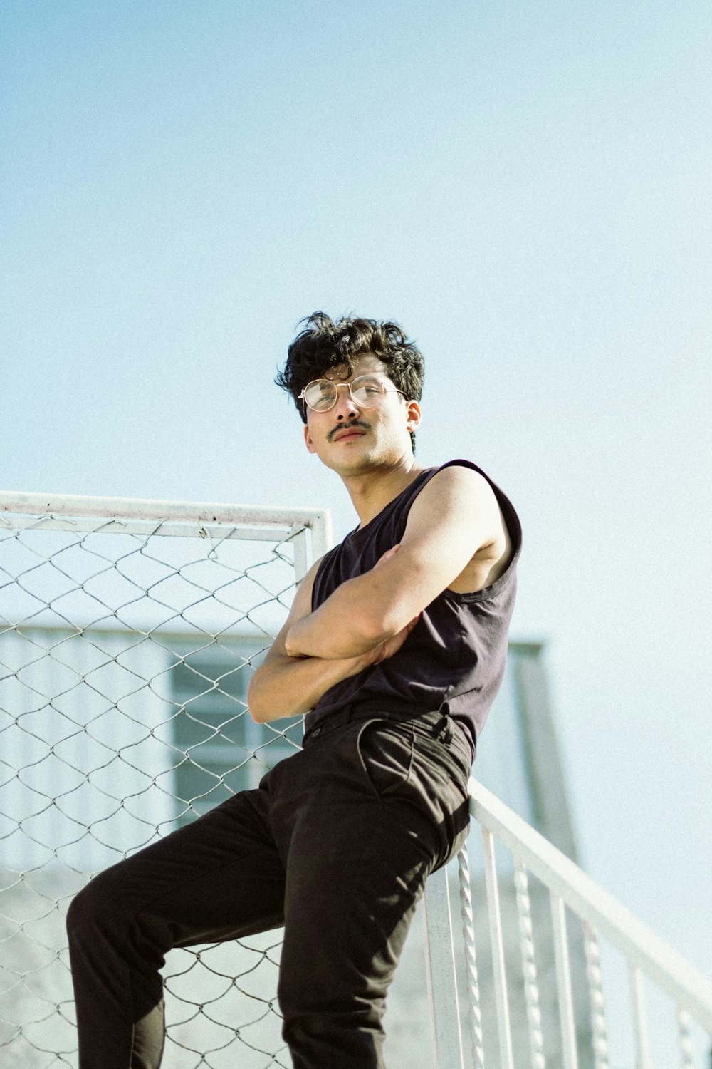 man in black tank top and black pants sitting on white metal fence