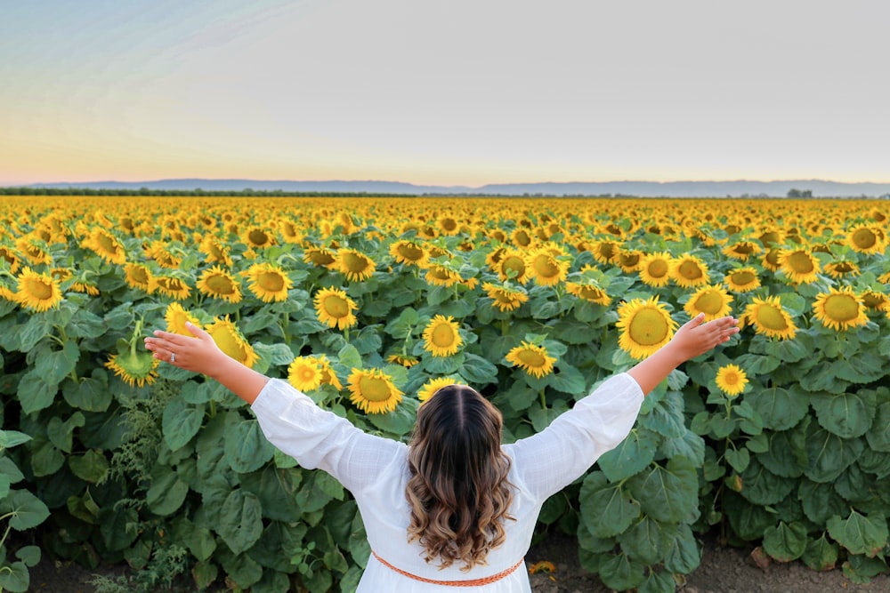 Frau im weißen Langarmhemd tagsüber auf Sonnenblumenfeld stehend