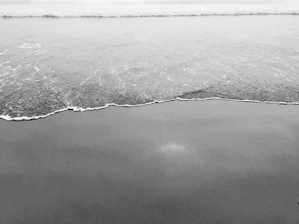A serene black and white photograph capturing the gentle waves meeting the sandy shore in exquisite detail.