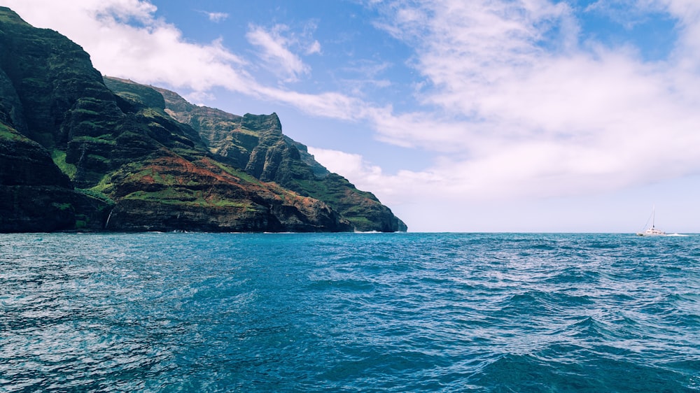 green and brown mountain beside blue sea under blue sky during daytime