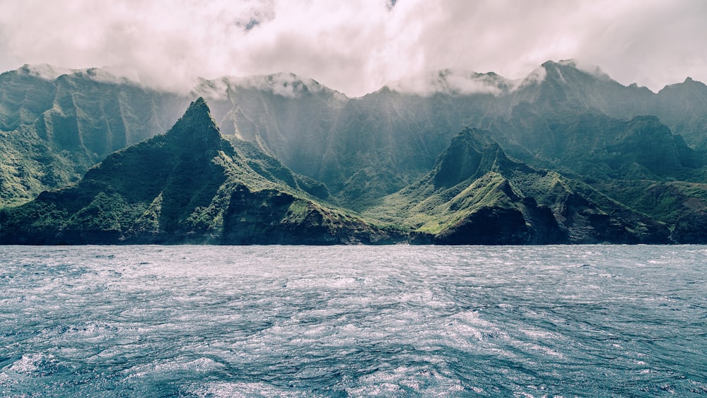 body of water near mountain under cloudy sky during daytime