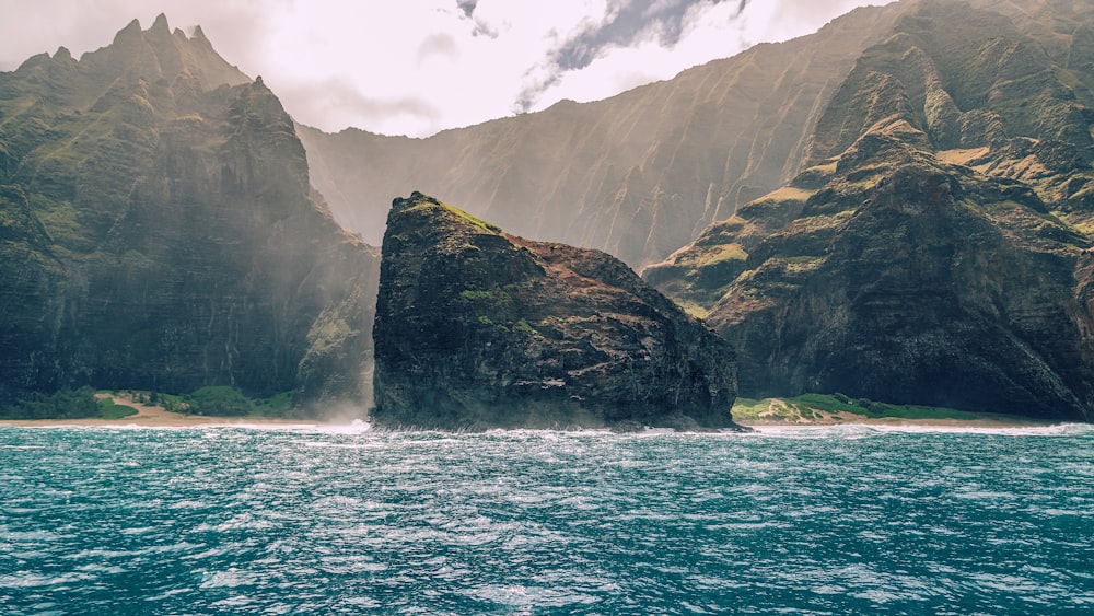 green and brown mountain beside body of water under cloudy sky during daytime