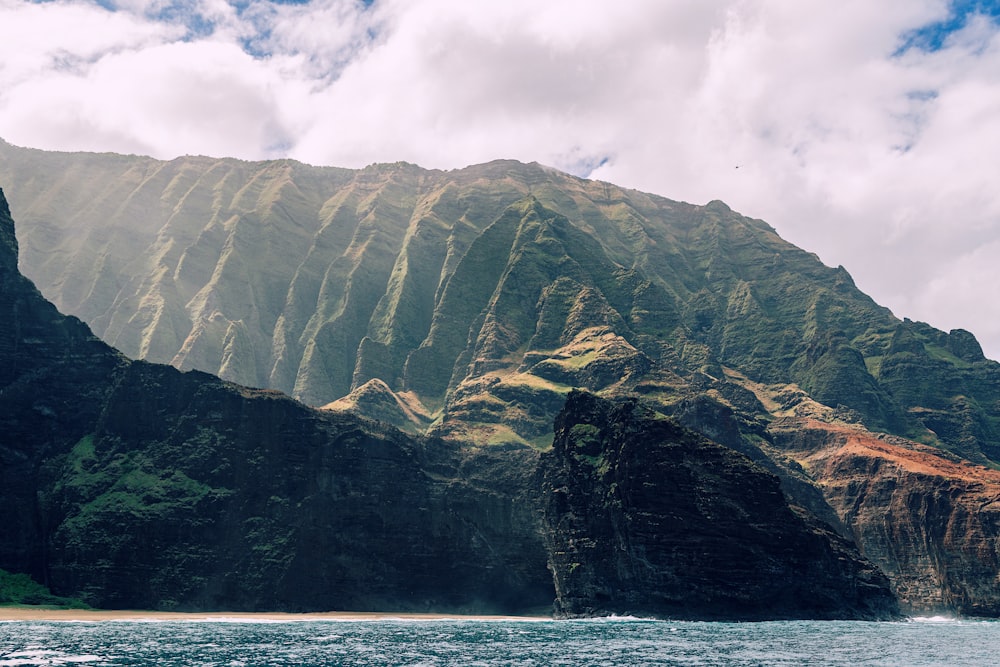 green and brown mountain beside body of water during daytime