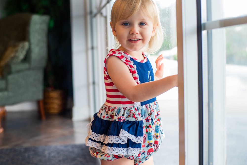girl in red and white striped tank top and floral skirt standing beside glass window during