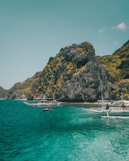 white boat on sea near green and brown rock formation under blue sky during daytime in El Nido Philippines