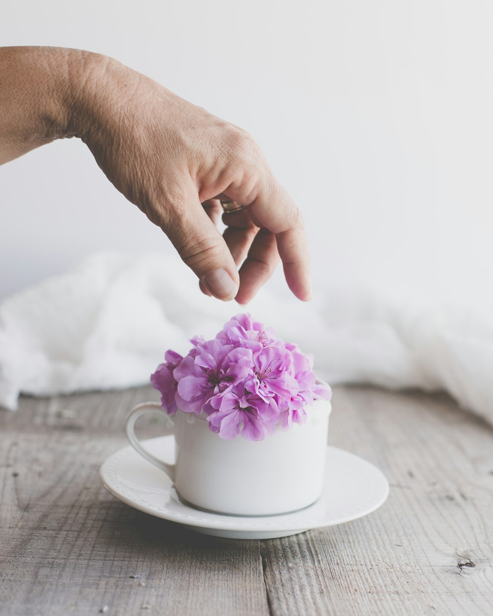 紫色の花が描かれた白い陶器のマグカップを持っている人