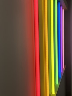 A series of colorful vertical light tubes arranged in a row, emitting vibrant hues. The scene includes shades of red, orange, yellow, green, blue, and violet, creating a striking visual effect against a plain background.