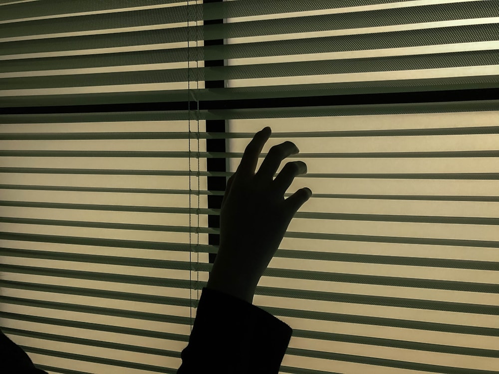 persons left hand on white window blinds
