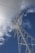 A tall metal power transmission tower stands against a backdrop of a partially cloudy blue sky. Power lines extend outwards from the tower, creating a network of cables in the sky.
