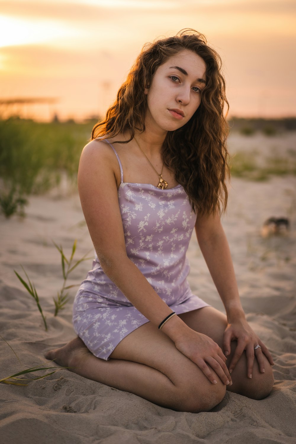 woman in white spaghetti strap dress sitting on sand during sunset