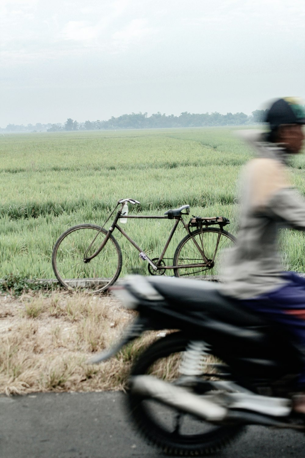 man in gray shirt riding on black bicycle on green grass field during daytime