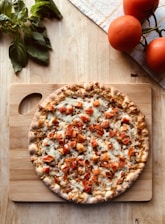 A vibrant pizza topped with fresh basil, melted mozzarella, and ripe tomatoes on a rustic wooden table.