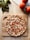 A freshly baked pizza topped with diced tomatoes and melted cheese sits on a wooden cutting board. Fresh basil leaves and ripe tomatoes are placed nearby on a light wooden surface, giving a rustic kitchen ambiance.