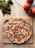 A freshly baked pizza topped with diced tomatoes and melted cheese sits on a wooden cutting board. Fresh basil leaves and ripe tomatoes are placed nearby on a light wooden surface, giving a rustic kitchen ambiance.