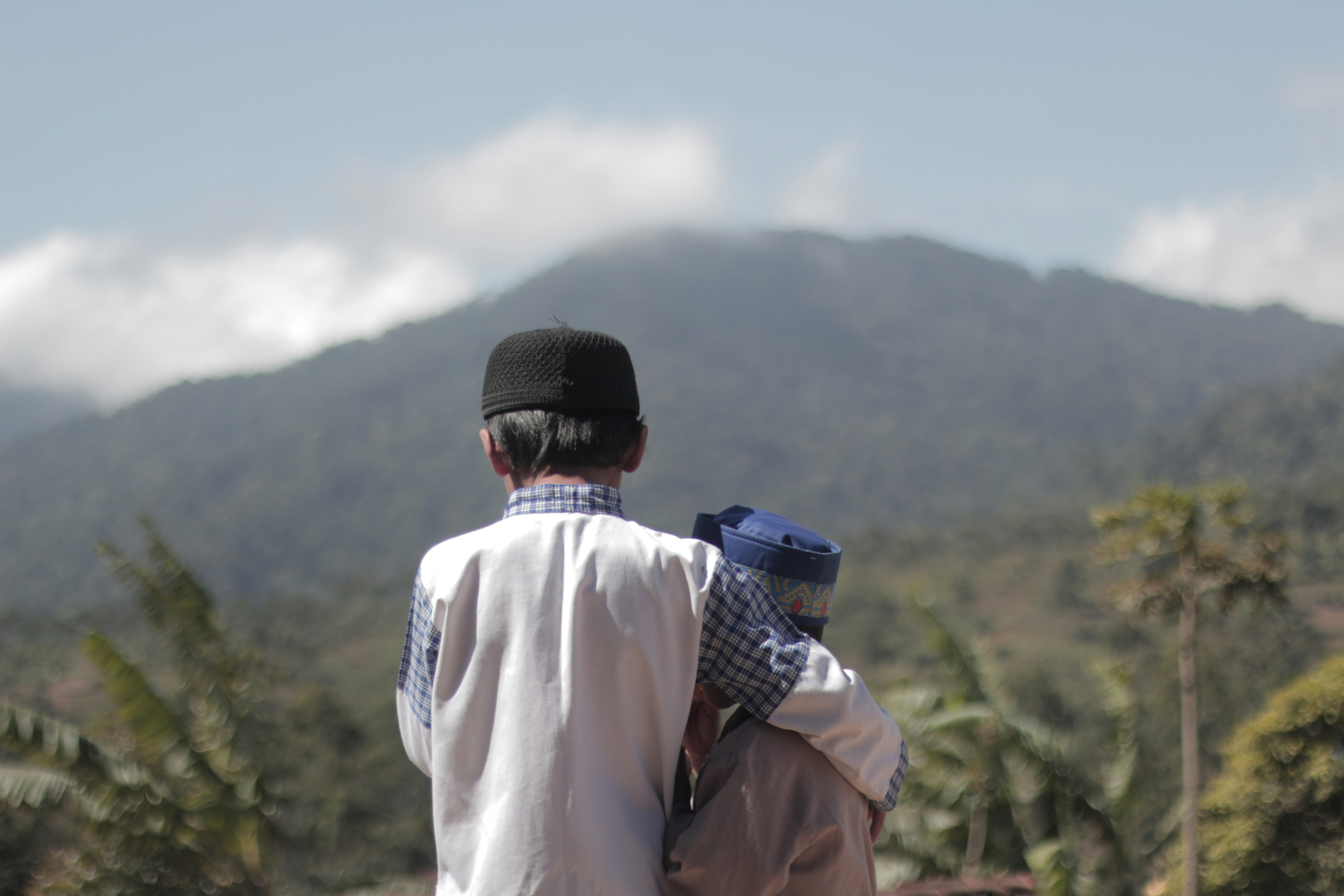 Pria dengan jaket putih dan topi rajutan hitam melihat pegunungan di siang hari