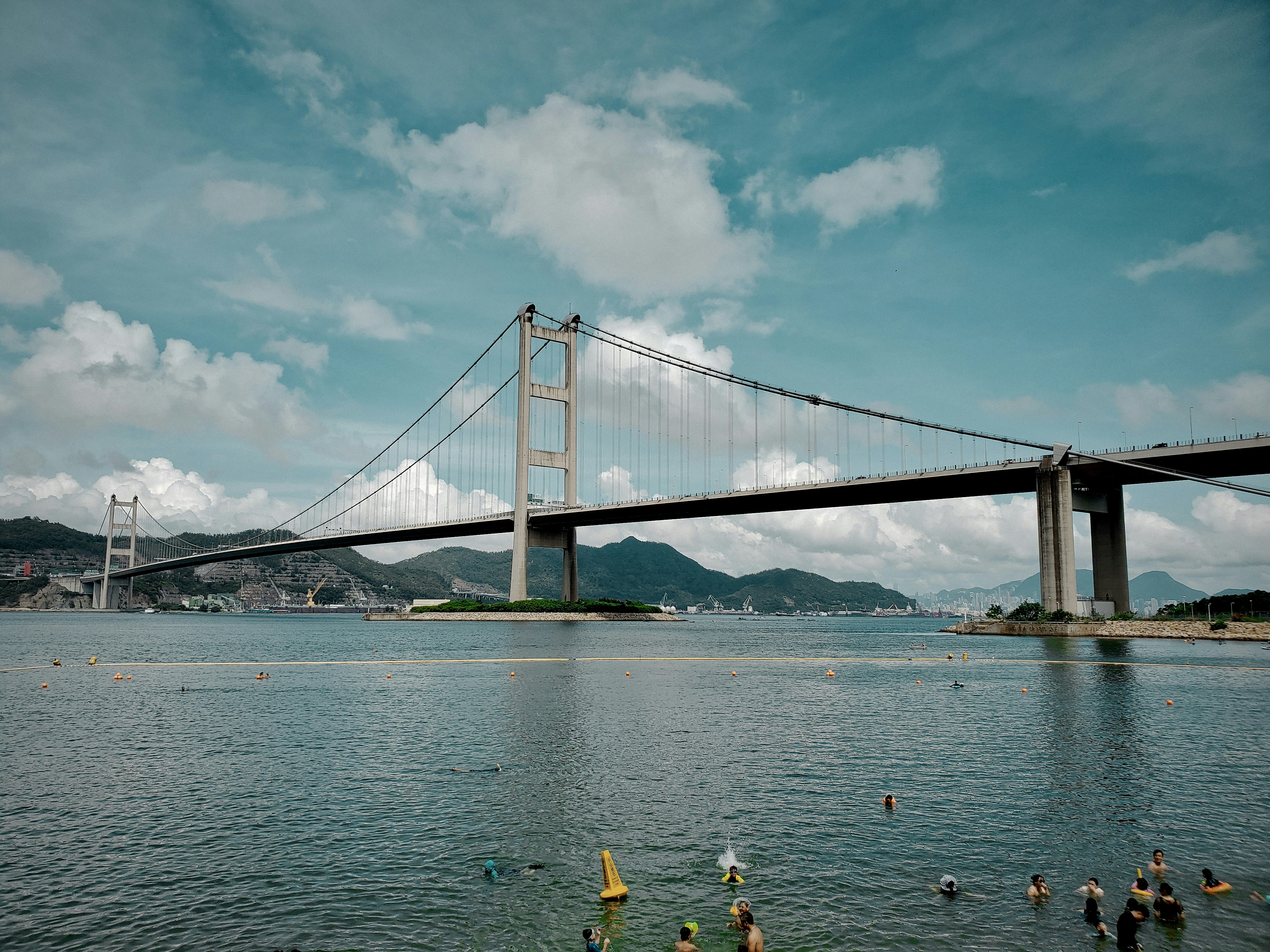 people riding on yellow kayak on sea near bridge under white clouds and blue sky during