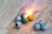 A collection of small spherical fireworks is arranged on a wooden surface. One of the fireworks is lit, emitting bright sparks and a burst of light. The spheres are in various colors, including gray, green, blue, and yellow, some with visible fuses.