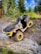 A rugged all-terrain vehicle with yellow accents is parked on a rocky, inclined surface surrounded by lush greenery and trees. The vehicle's large tires and sturdy design suggest it is equipped for off-road adventures.