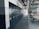 A spacious office or industrial storage space with large metal cabinets lined up along the wall, featuring circular locks. The area also includes modern office chairs and workstations with orange accents. Overhead, there is an array of exposed pipes and ventilation ducts.