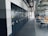 A spacious office or industrial storage space with large metal cabinets lined up along the wall, featuring circular locks. The area also includes modern office chairs and workstations with orange accents. Overhead, there is an array of exposed pipes and ventilation ducts.