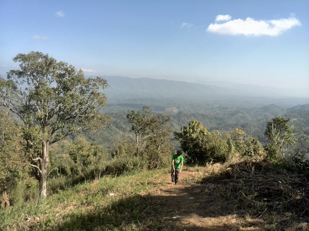 person in green jacket walking on dirt road near green trees during daytime